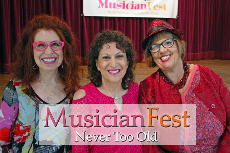 Three mature women smiling. They are dressed in shades of pink and red. A banner with the words Musician Fest appears behind them.