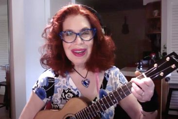 a woman with red hair, glasses, and a ukulele